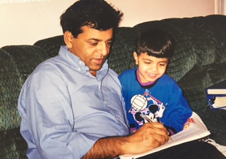A man and a young boy sitting together on a sofa, writing in a notebook.