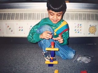 A young boy sitting on a carpet, carefully stacking colourful blocks into a tower.