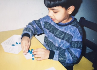 A young boy at a small table sorting blue counters into a tray.