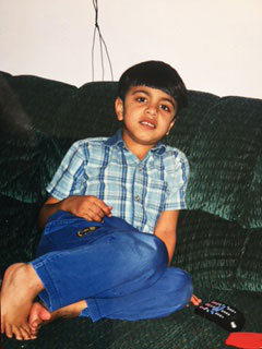 Qasim sitting on a sofa in a checked shirt, looking at the camera.