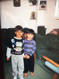Two boys standing side by side in front of a sofa, both looking toward the camera.