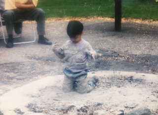 Qasim kneeling in a sandy patch at a playground, absorbed in the sand.
