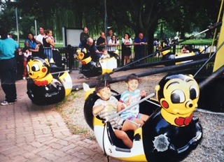 Two children riding side by side on a bee-shaped ride at an amusement area.