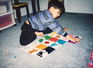 Qasim leaning across a colourful picture-matching mat laid out on the floor.
